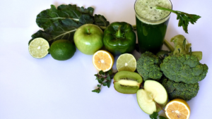 Suco detox verde acompanhado por ingredientes frescos como maçã verde, pimentão verde, brócolis, limões, kiwi e folhas de couve.