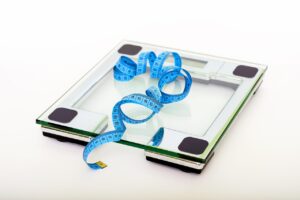 Balança digital com fita métrica azul, representando controle de peso saudável no pós-parto.