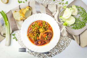 A imagem apresenta um ensopado nutritivo à base de legumes e ervilhas, com molho rico em cor e sabor. O prato está acompanhado por pão fresco e vegetais crus, compondo uma refeição equilibrada e aconchegante. É uma inspiração para quem busca receitas simples, saudáveis e repletas de sabor caseiro.
