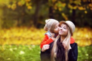 Mãe sorridente recebendo beijo do filho em um dia de outono, simbolizando amor e bem-estar no pós-parto.