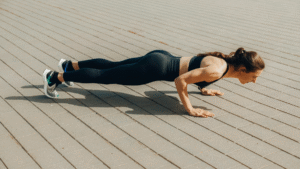 Mulher praticando exercício de flexão no chão de concreto, usando roupa esportiva preta