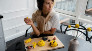 Mulher sentada à mesa saboreando manga com frutas vermelhas e mirtilos ao lado