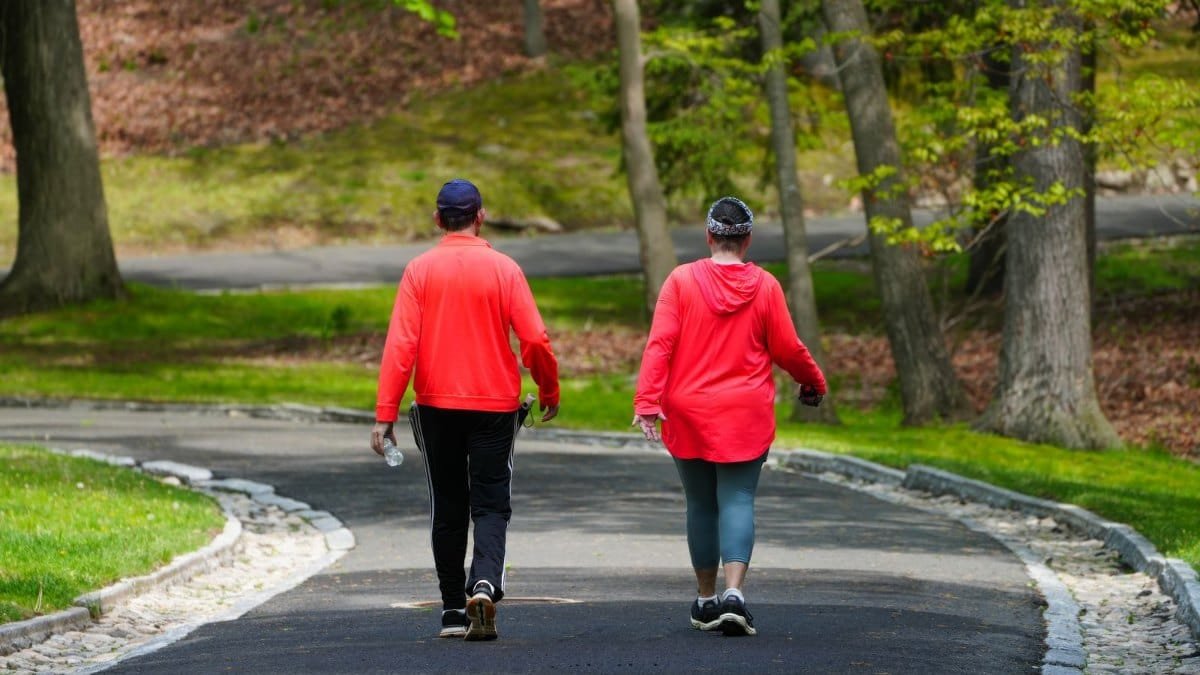 Duas pessoas de costas caminhando em passo firme por um caminho de parque cercado de árvores