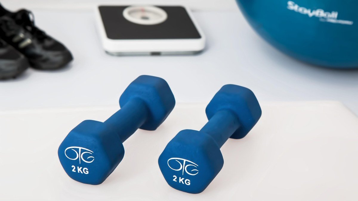 Dois halteres azuis de 2 kg ao lado de uma balança digital e tênis esportivos