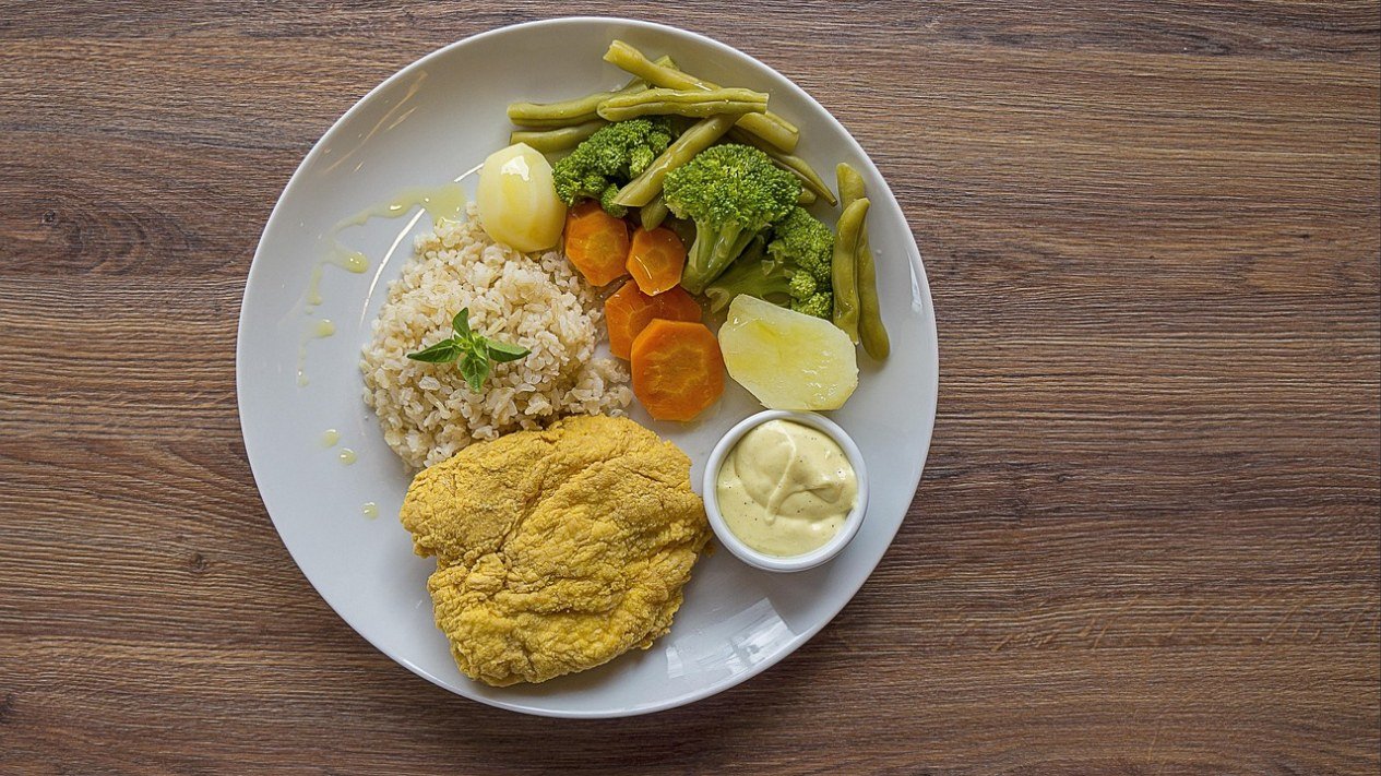 Prato visto de cima com arroz, brócolis, cenoura, vagem, batata e um filé de frango, exemplo de refeição para uma dieta normocalórica