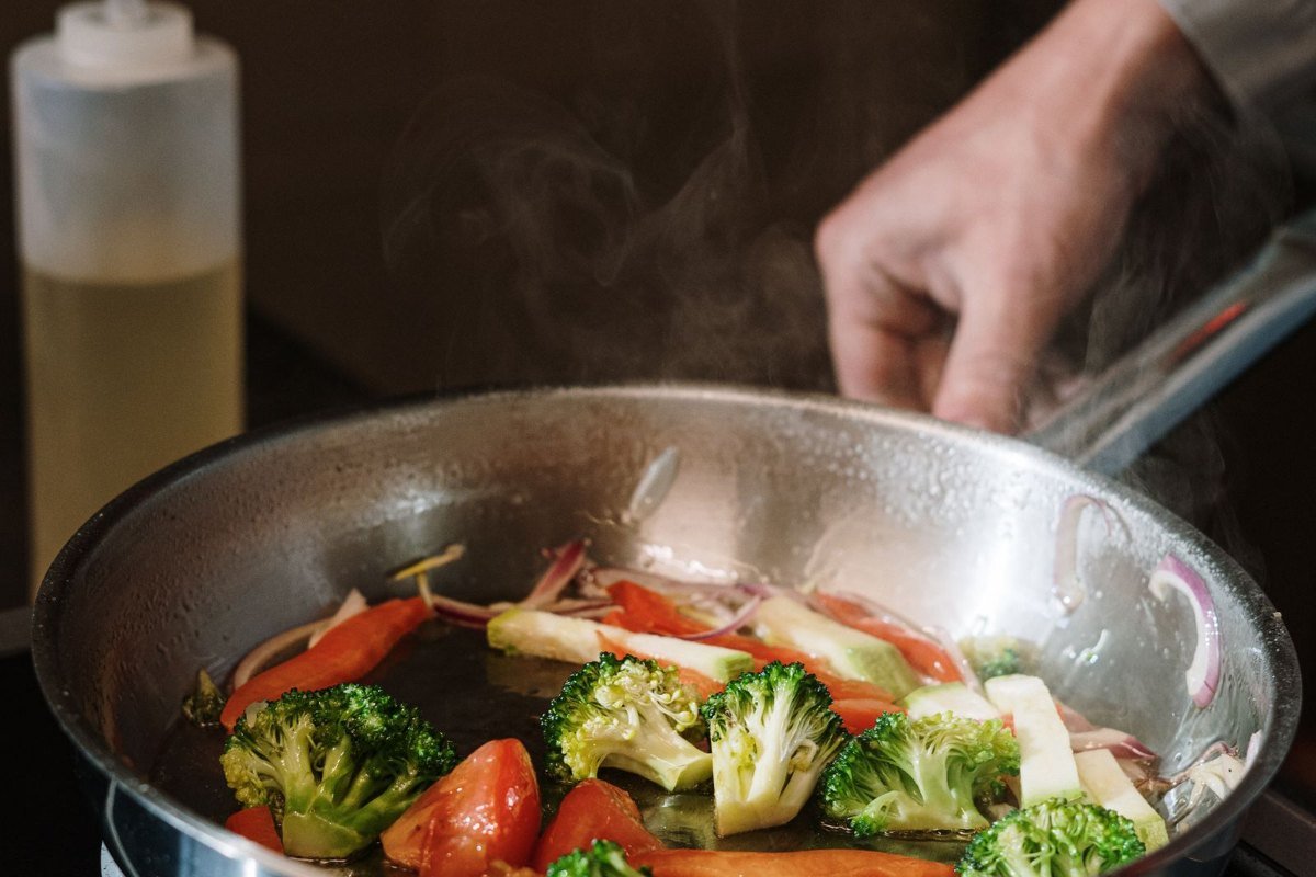 Pessoa segurando uma frigideira preta com legumes salteados, refeição simples feita em casa