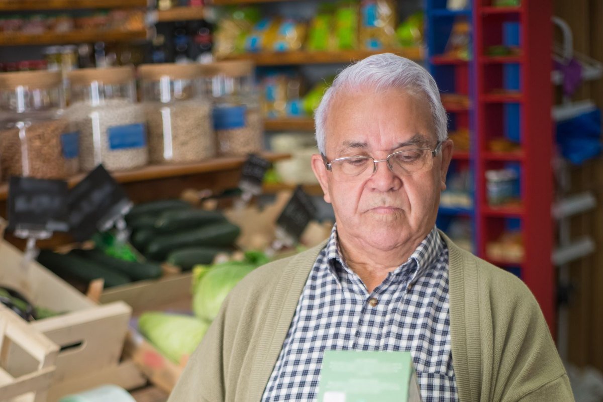 Homem de cardigã olhando a embalagem de um produto no mercado