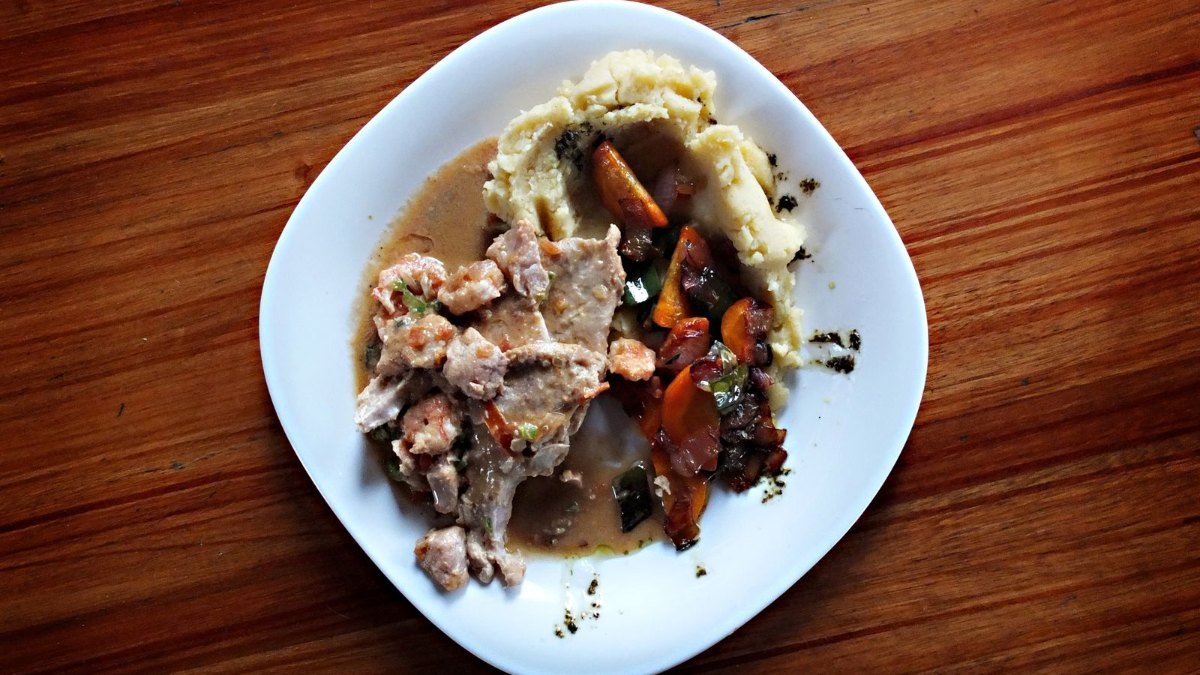 Prato com carne, legumes e purê de batata sobre uma mesa de madeira, visto de cima