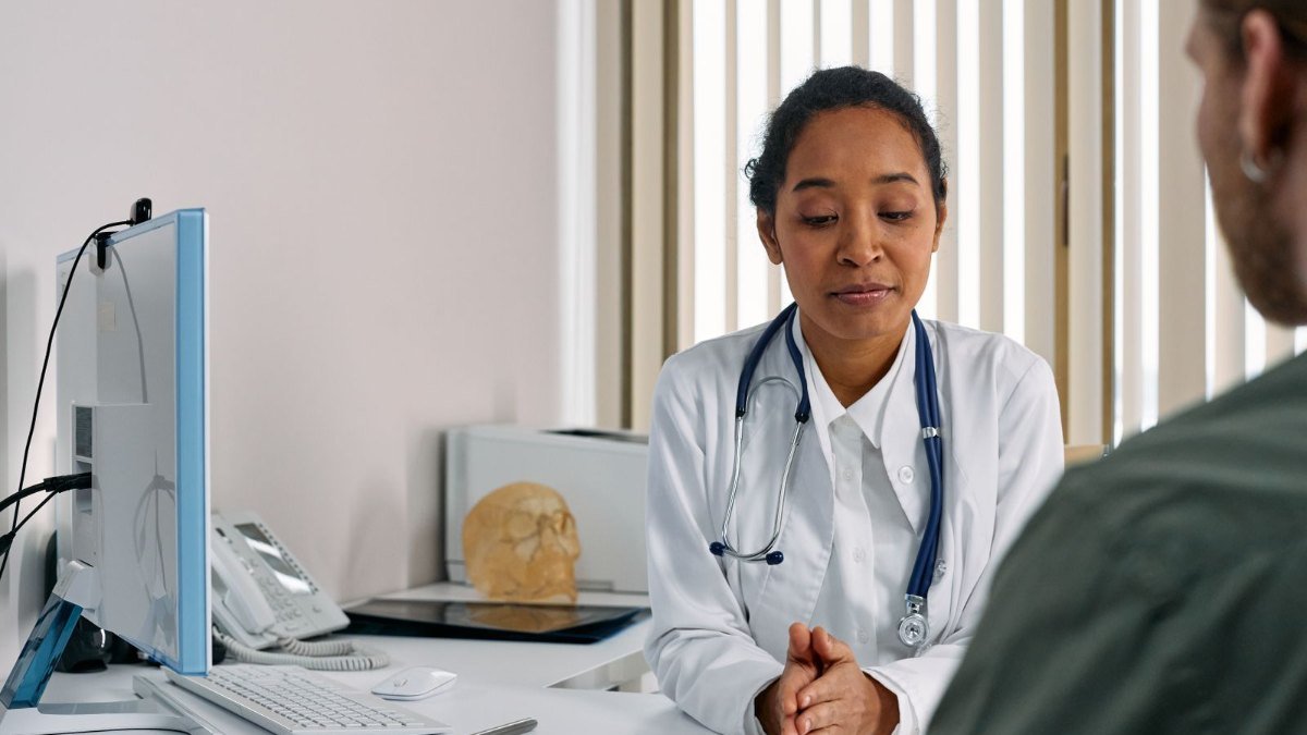 Médica de jaleco branco com estetoscópio conversando com um paciente em um consultório, avaliação que vem antes de decidir como eliminar gordura no fígado
