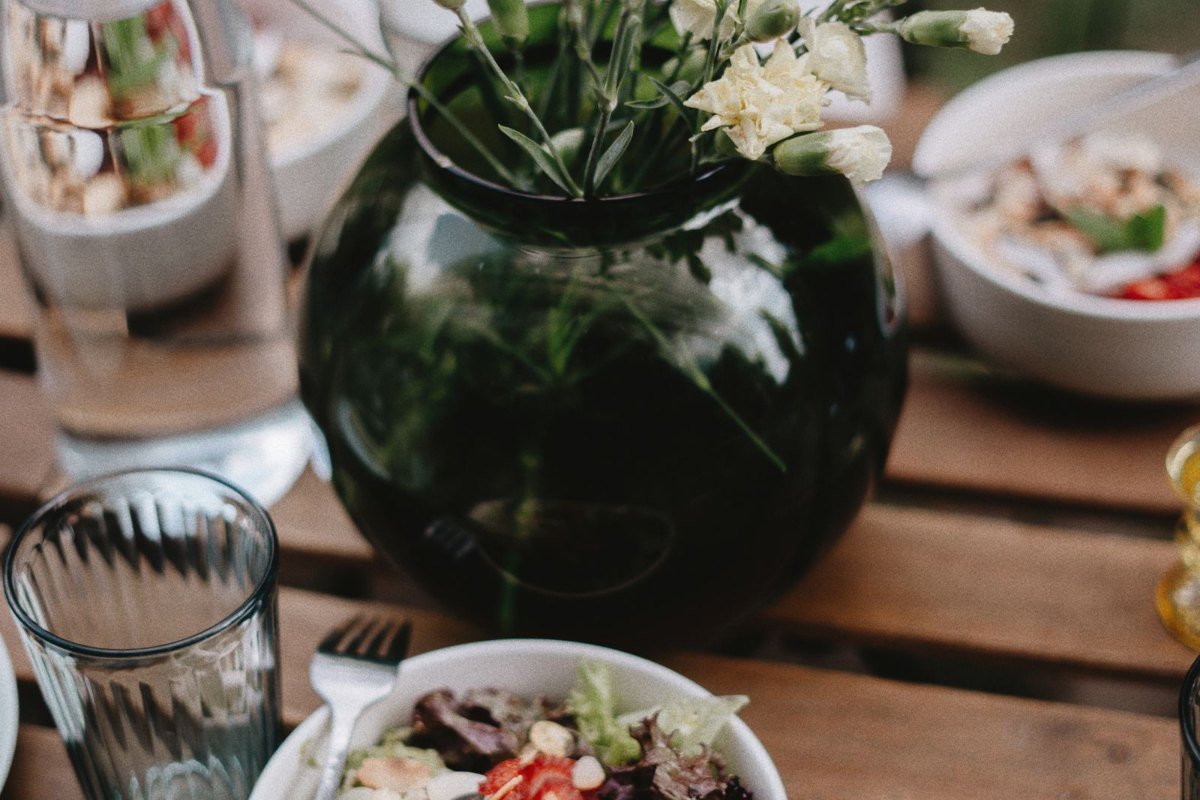 Mesa com tigelas de salada e legumes, vaso de flores e copos de água