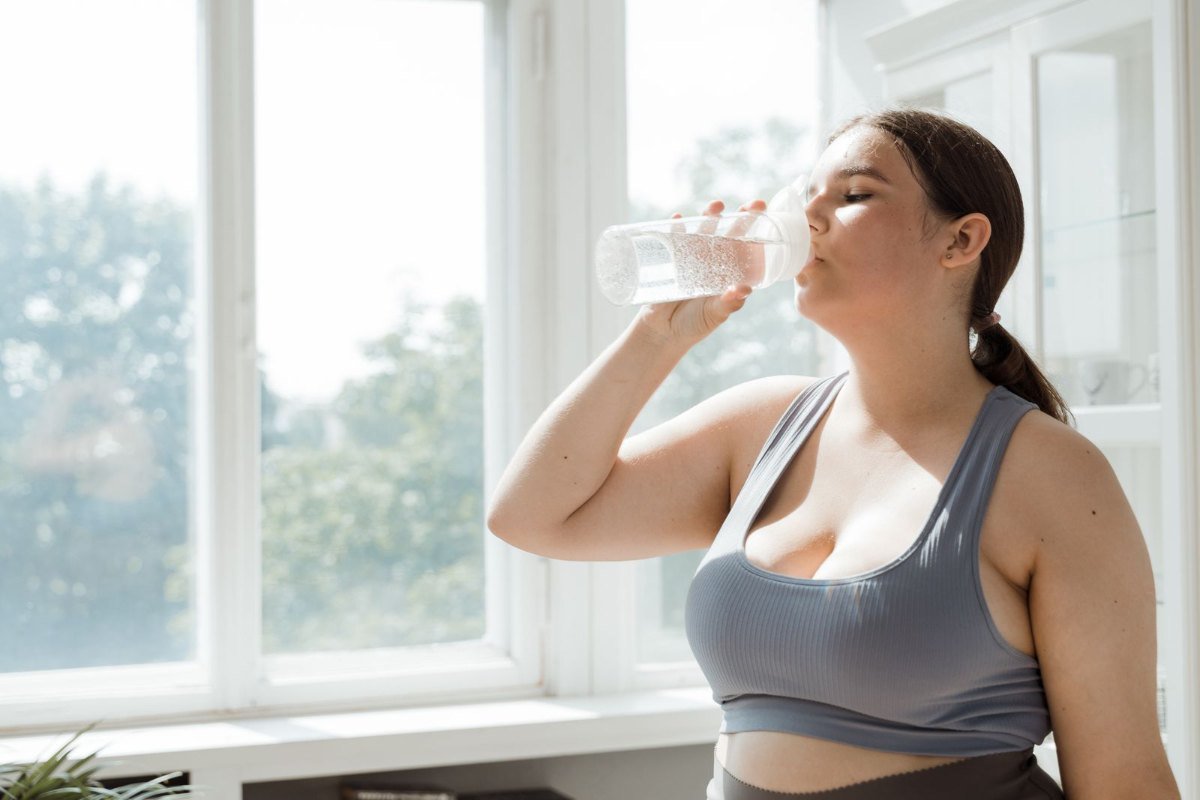 Mulher de roupa esportiva bebendo água: beber água ajuda a emagrecer quando faz parte da rotina