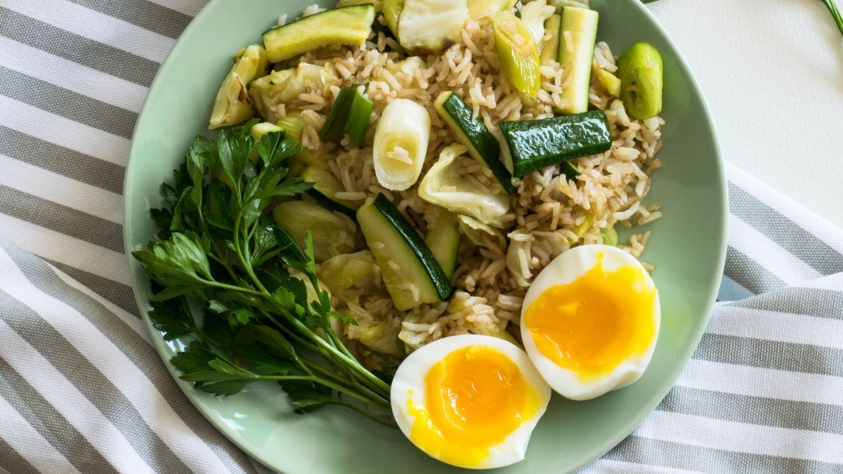 Prato verde com arroz, abobrinha, salsa e ovos cozidos cortados ao meio, com a gema mole