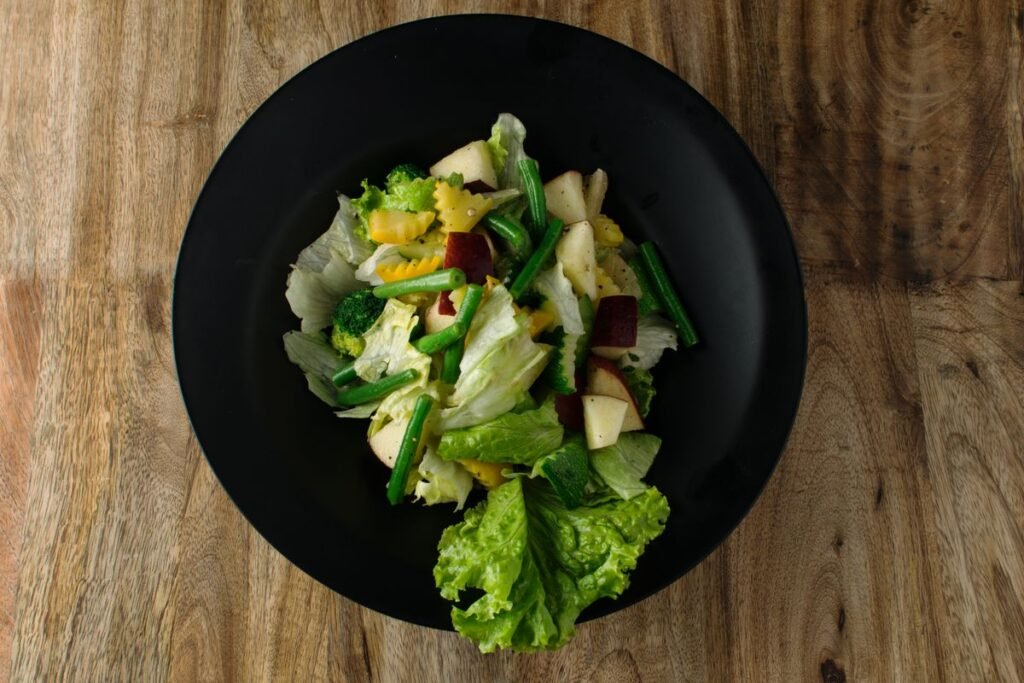 Prato preto com salada de folhas verdes e legumes sobre uma mesa de madeira