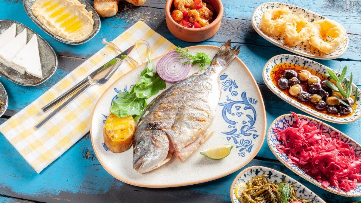 Mesa com peixe grelhado, azeitonas, queijo e saladas, refeição no estilo mediterrâneo que as diretrizes citam para quem quer eliminar gordura no fígado