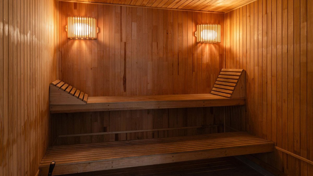 Interior de uma sauna de madeira com bancos em dois níveis e duas luminárias acesas nas paredes