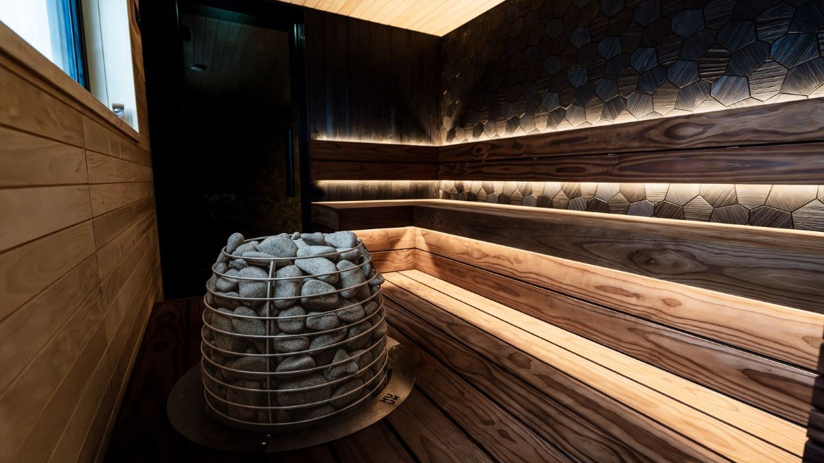 Interior de uma sauna moderna com bancos de madeira e aquecedor de pedras, onde muita gente pergunta se a sauna ajuda a emagrecer