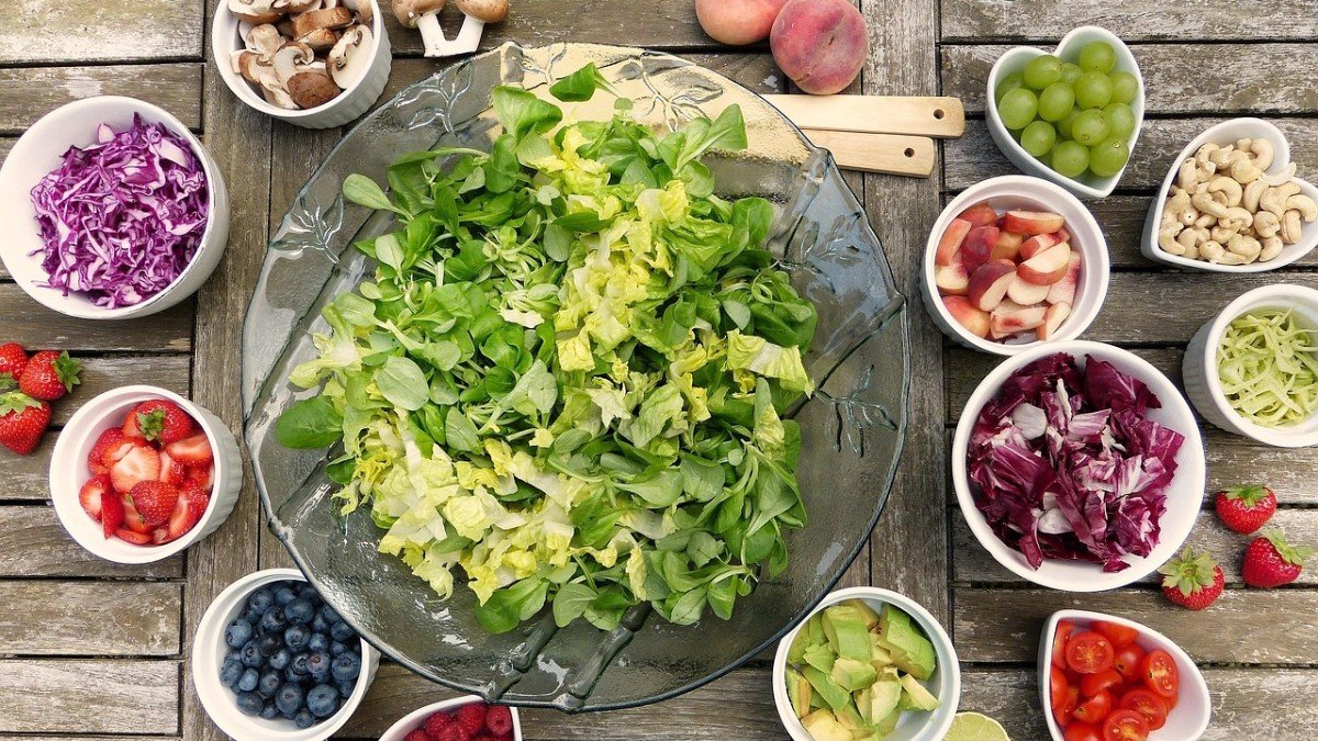 Tigelas de salada, frutas e oleaginosas Mesa de madeira com tigelas de salada verde, repolho roxo, morangos, mirtilos, tomates, abacate e castanhas